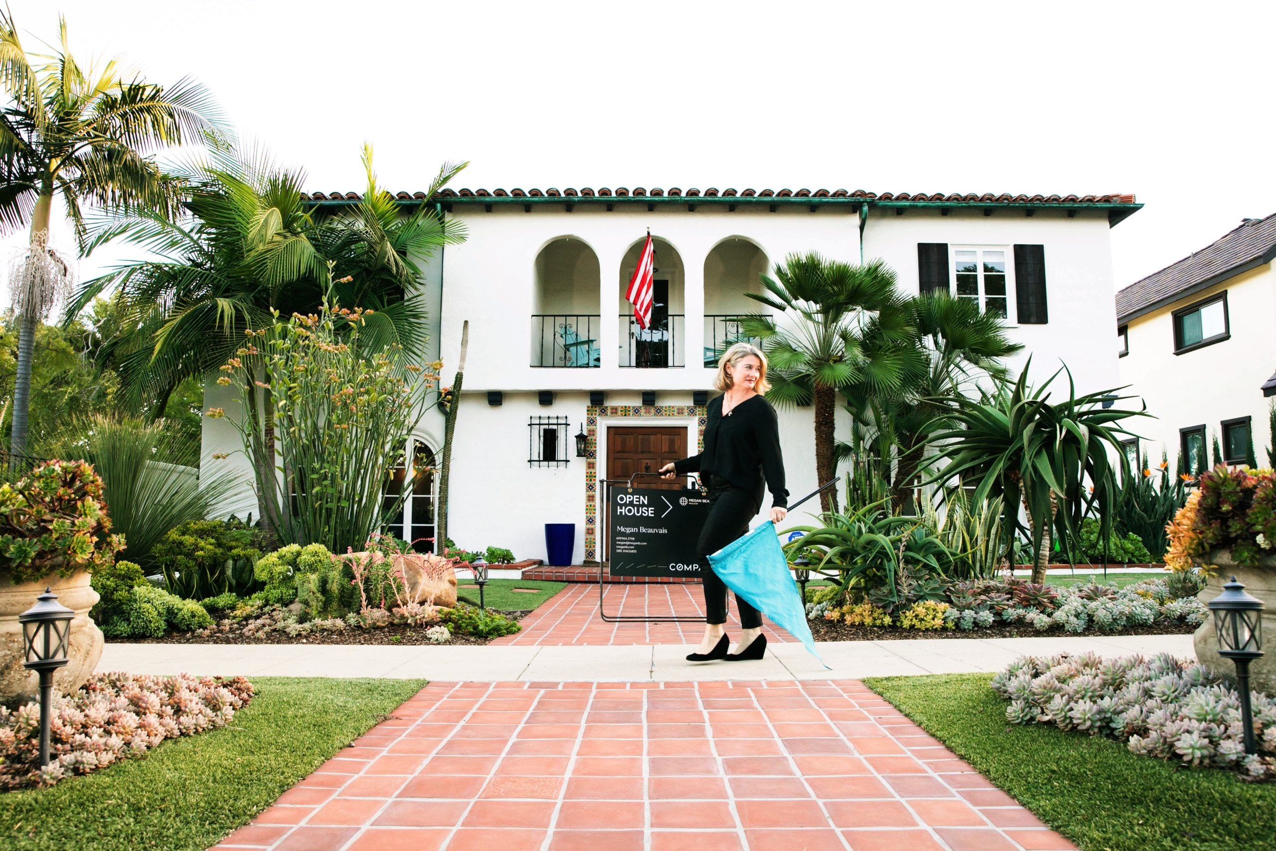 Megan Beauvais in front of a San Diego Home holding one of her Compass Real Estate Signs